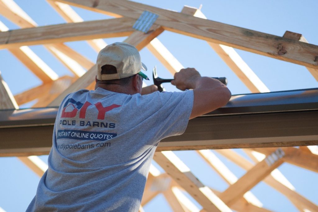 A man wearing a DIY Pole Barns shirt constructing a pole barn.