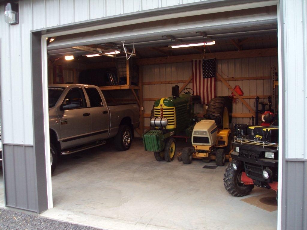 A pickup truck, tractor, and other equipment are parked in a pole barn with concrete pole barn flooring