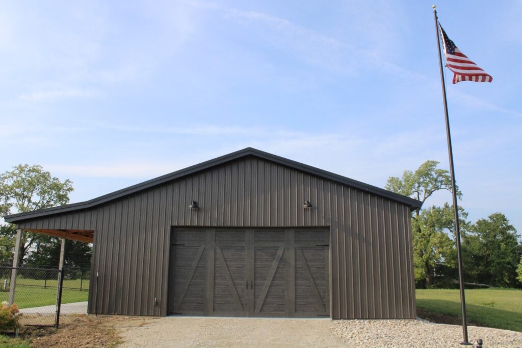 A brown pole barn front with large barn doors and an American flag raised high on a pole